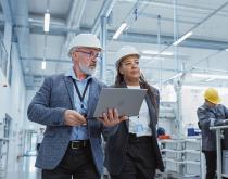 Two employees on manufacturing plant floor carrying a laptop