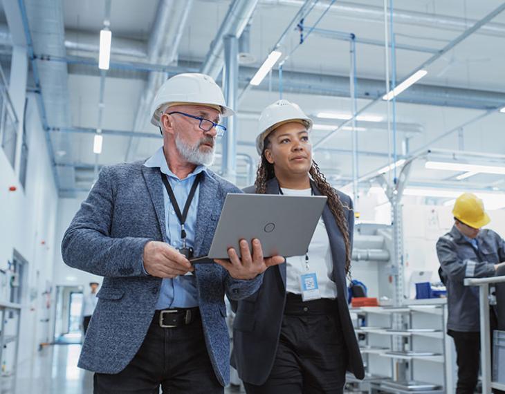 Two employees on manufacturing plant floor carrying a laptop